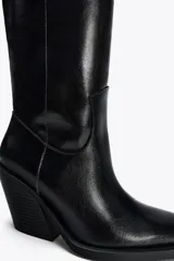 Bota alta de cuero sintético color negro, estilo cowboy, con puntera fina, tiradores laterales y tacón geométrico.