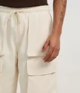 Bermuda baggy color crema, confeccionada en algodón y poliéster. Cuenta con cintura elástica ajustable con cordón y bolsillos cargo laterales.