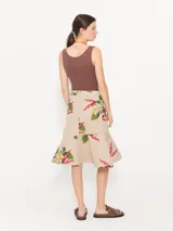 Pollera midi de gabardina color beige con estampado de flores y bordados. Presenta un cruce diagonal con botón dorado personalizado y botón interno para sostener la solapa inferior. Incluye bolsillo plaqué en delantero orientado a cintura y volado en forma de caracol en el ruedo.