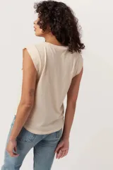 Muscle tank de jersey de algodón suave, color beige claro, con sisas terminadas y calce relajado. Presenta un gráfico vintage en color rosado con una botella de champagne y copas, y el texto "Champagne Brunch without it".