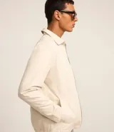 Campera color crema de sarga lisa, con cuello camisero, cierre frontal con cremallera, bolsillos delanteros, puños abotonados y bajo elástico.