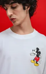 Remera oversize de algodón premium color blanco, con cuello redondo y manga corta. Presenta un pequeño estampado del personaje Mickey Mouse en el lado izquierdo del pecho.