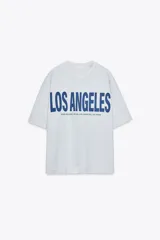 Camiseta gris jaspeado de corte amplio, cuello redondo y mangas cortas. Estampado frontal con la frase "Los Angeles 8500 Beverly Blvd, Los Angeles, CA 90048" en color azul.