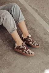 Zapatillas bajas con estampado animal print en blanco y marrón, con detalles en cuero marrón en los laterales y cordones marrones. Suela de goma color caramelo y forro interior color crema.