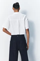 Camisa celeste de popelín con cuello solapa, escote pico y manga corta. Presenta dos bolsillos delanteros de parche y cierre frontal con botones.