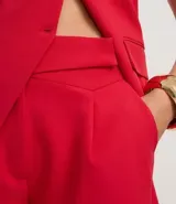 Bermuda sastre de poliéster color rojo, de tiro alto, con cintura asimétrica cruzada, pliegues frontales y bolsillos laterales.