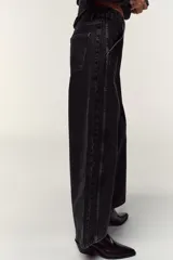 Pantalón de jean negro con lavado gastado, corte culotte, tiro alto, bolsillos delanteros y traseros, y cierre frontal con cremallera y botón.