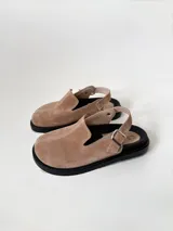 Zuecos color beige de cuero gamuzado, con punta cerrada, suela de goma negra y tira trasera con hebilla metálica.