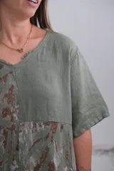 Blusa verde militar con estampado de hojas en tonos marrones y blancos, cuello en V y mangas cortas.