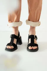 Sandalias negras de charol con tiras entrecruzadas, hebilla dorada y tacón de madera.