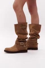 Bota de caña alta color negro, confeccionada en gamuza, con dos correas desmontables con hebillas metálicas.