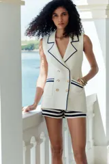 Top chaleco color crema con cuello solapa, sin mangas, doble botonadura dorada y bolsillos delanteros con ribete azul marino.