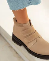 Botín corto de cuero color visón (beige/topo), con cierre de tres tiras de velcro en el empeine. Posee cuello acolchado de gamuza y suela de goma negra con relieve tractor.