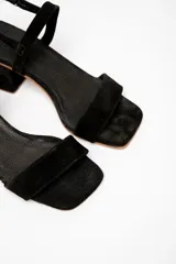 Sandalias negras de cuero gamuzado, con tira fina sobre los dedos y tobillo, y taco cuadrado bajo.