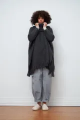 Poncho tejido de lana color gris oscuro, con cuello alto y flecos en el ruedo.