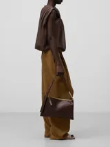 Bolso de hombro plano de cuero color marrón oscuro, con asa corta regulable con anilla metálica dorada. Tiene un compartimento con cierre de cremallera y bolsillo interior.