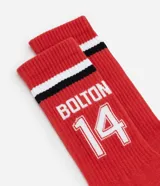 Par de medias rojas de caña alta con rayas horizontales blancas y negras en el borde superior. Estampado con el nombre "Bolton" y el número 14 en blanco.