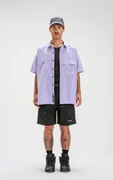 Camisa de manga corta color lavanda con doble bolsillo y ojal delantero con solapa en uno de ellos. Tiene calce oversize y está realizada en tejido plano suave al tacto.