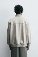 Cazadora color gris claro de corte regular, confeccionada en tejido con efecto ante. Tiene cuello alto, cierre frontal con cremallera, bolsillos laterales y puños y bajo en rib elástico.