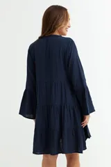 Vestido corto azul marino de manga larga con puños acampanados. Presenta un diseño escalonado con volados y escote en V con botones. El tejido parece ser de gasa o algodón texturizado.