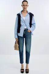 Pantalón de jean azul de tiro alto, corte mom fit, tobillero y con cinco bolsillos. Cierre frontal con cremallera y botón.