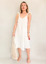 Vestido blanco de lino con breteles finos que se atan en los hombros. Corte suelto y largo midi.