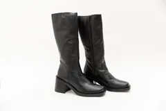 Bota de caña alta de cuero negro, con punta cuadrada y taco bloque. Presenta cierre lateral.