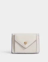 Billetera pequeña color blanco con textura granulada y detalles en lila. Tiene solapa con broche de corazón dorado y botón a presión.