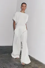 Pantalón palazzo color crudo, confeccionado en hilatura con mezcla de lyocell. Tiro medio, cintura elástica ajustable con cordones, bolsillos laterales ocultos en costura y pierna ancha.