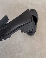 Mocasines negros con suela track y detalle de antifaz con textura croco.