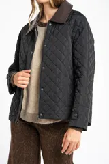 Campera capitoneada de color negro con diseño de rombos, cuello camisero en contraste de color marrón, cierre frontal con cremallera y solapa con botones a presión. Presenta mangas largas con puños ajustables y un calce entallado.