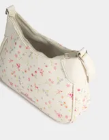 Bandolera tipo baguette de cuerina color blanco con estampado de flores pequeñas en tonos rosa y lila. Tiene manija superior, cierre superior y tag de metal.