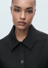 Chaqueta corta de color negro, con cuello camisero, cierre frontal de botones y bolsillos de parche.