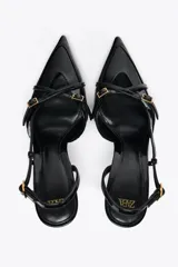 Zapato de tacón fino color negro charol, con punta fina, tiras cruzadas y hebilla ajustable en el tobillo.