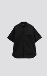 Camisa negra de manga corta, corte oversize, confeccionada en poplin 100% algodón. Presenta dos bolsillos delanteros, uno con solapa y otro con ojal y botón.