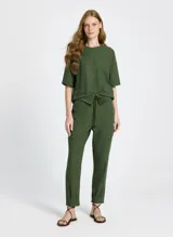 Remera verde militar de tejido de punto con corte recto, cuello redondo y mangas cortas. Presenta bolsillos delanteros alargados con solapas y botones, bajo largo y acabado pespunteado.