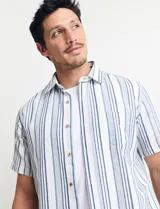 Camisa de manga corta a rayas verticales color natural y azul, con cuello clásico y cierre frontal con botones.