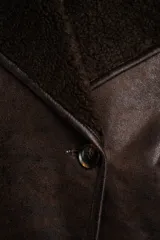 Chaqueta tipo gamulán de calce oversize en color marrón oscuro, con exterior de poliéster y forro de corderito sintético. Presenta cuello de solapa ancha y cierre frontal con botones.