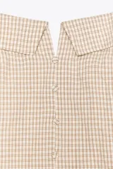 Vestido corto a cuadros beige y blanco, con cuello halter que se ata en la nuca, escote recto con abertura y falda acampanada. Tiene bolsillos laterales ocultos, espalda elastizada y botones decorativos en el frente.