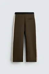 Pantalón jogger color verde oliva, corte relaxed fit, con cintura elástica ajustable con cordón, bolsillos laterales y detalle de bolsillo de vivo en la espalda. Presenta una banda lateral color crema a contraste.