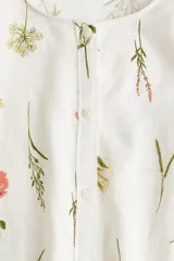 Blusa de lino color blanco con estampado de flores, cuello redondo, cierre de botones y mangas globo tres cuartos con puños elásticos.