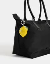 Llavero con dije de limón amarillo cubierto de strass y hoja verde. Incluye mosquetón metálico plateado para colgar en carteras, mochilas o bolsos.