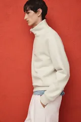 Buzo color crema de tejido pesado con interior cepillado, cuello elevado, medio cierre y hombros caídos. Puños y bajo en punto acanalado. Corte estándar.