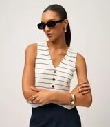 Chaleco sin mangas de punto, color blanco con rayas horizontales finas en negro. Presenta escote en V y cierre frontal con botones marrones.