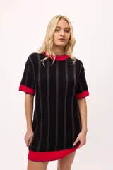 Vestido de tejido de punto, color negro con rayas verticales grises. Tiene cuello redondo y puños y ruedo en color rojo con costuras decorativas en hilo azul. Presenta un pequeño bordado de una letra 'B' estilizada en el pecho.