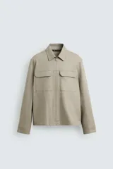Sobrecamisa color arena de corte relaxed fit, confeccionada en tejido con mezcla de algodón. Tiene cuello solapa, manga larga con puños abotonados, bolsillos de plastrón con solapa en el pecho y bolsillos laterales en la costura de la cadera. El cierre es frontal con cremallera.