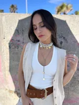 Gargantilla choker con hilo trenzado color blanco, adornada con conchas marinas tipo buzios y medallitas bañadas en oro y acero quirúrgico. Se cierra con cadena de acero quirúrgico y ganchito para ajustar el largo.