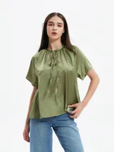 Camisa color verde oliva de mangas cortas, cuello redondo con lazo y corte holgado.