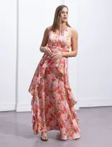Vestido largo de gasa estampada con flores en tonos naranja, rosa y lila. Tiene escote halter, busto plisado, corte en la cintura con faja plisada y falda con sobrecapa y forro interno a tono.