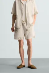 Bermuda regular fit color beige con bordados de flores en tono marrón. Tiene cintura elástica ajustable con cordón, bolsillos laterales y un bolsillo trasero de plastrón.